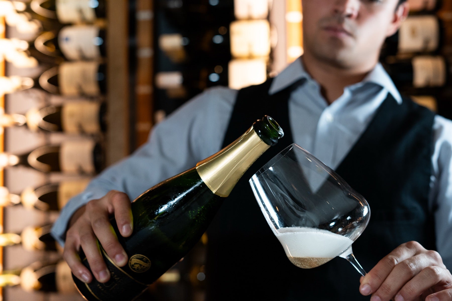 A sommelier pouring champagne in front of a wall of wine at a champagne and caviar evening